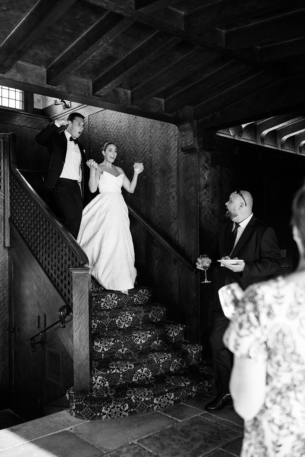 Black and white film photo of the newlyweds excitedly descending a wooden staircase for their grand entrance.